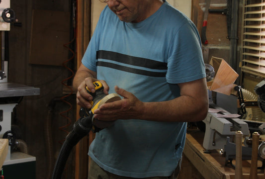 man using sander to sand down piece of wood in a workshop